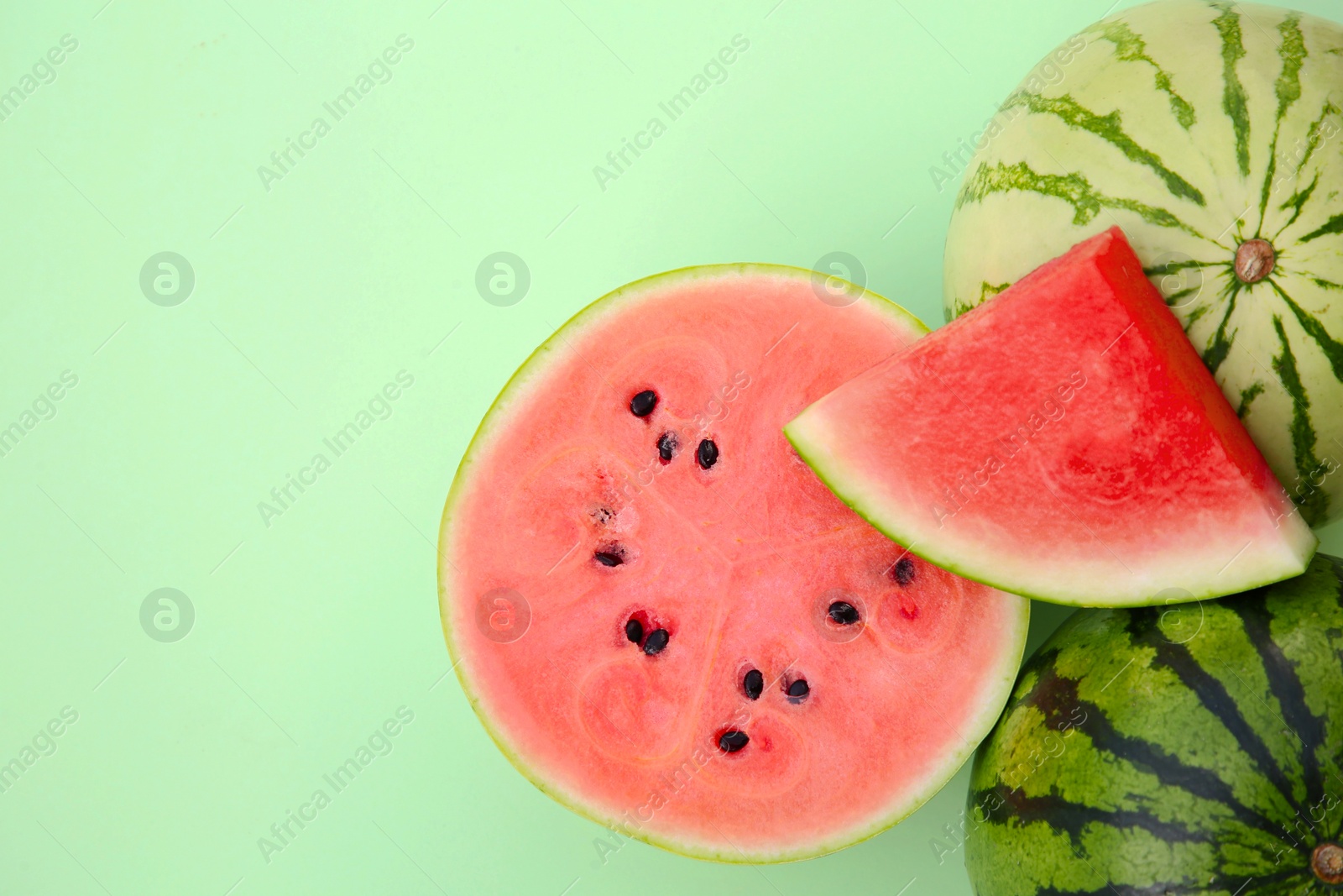 Photo of Different cut and whole ripe watermelons on light turquoise background, flat lay. Space for text