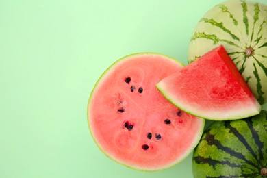 Different cut and whole ripe watermelons on light turquoise background, flat lay. Space for text