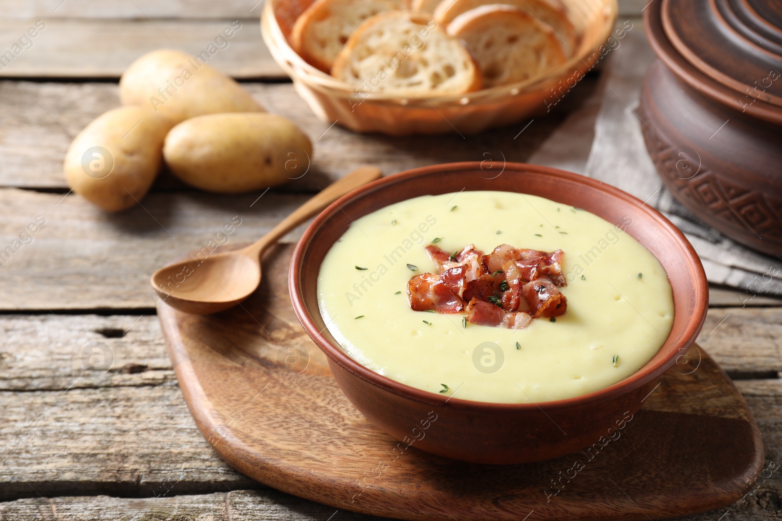 Photo of Tasty potato soup with bacon and rosemary in bowl served on wooden table