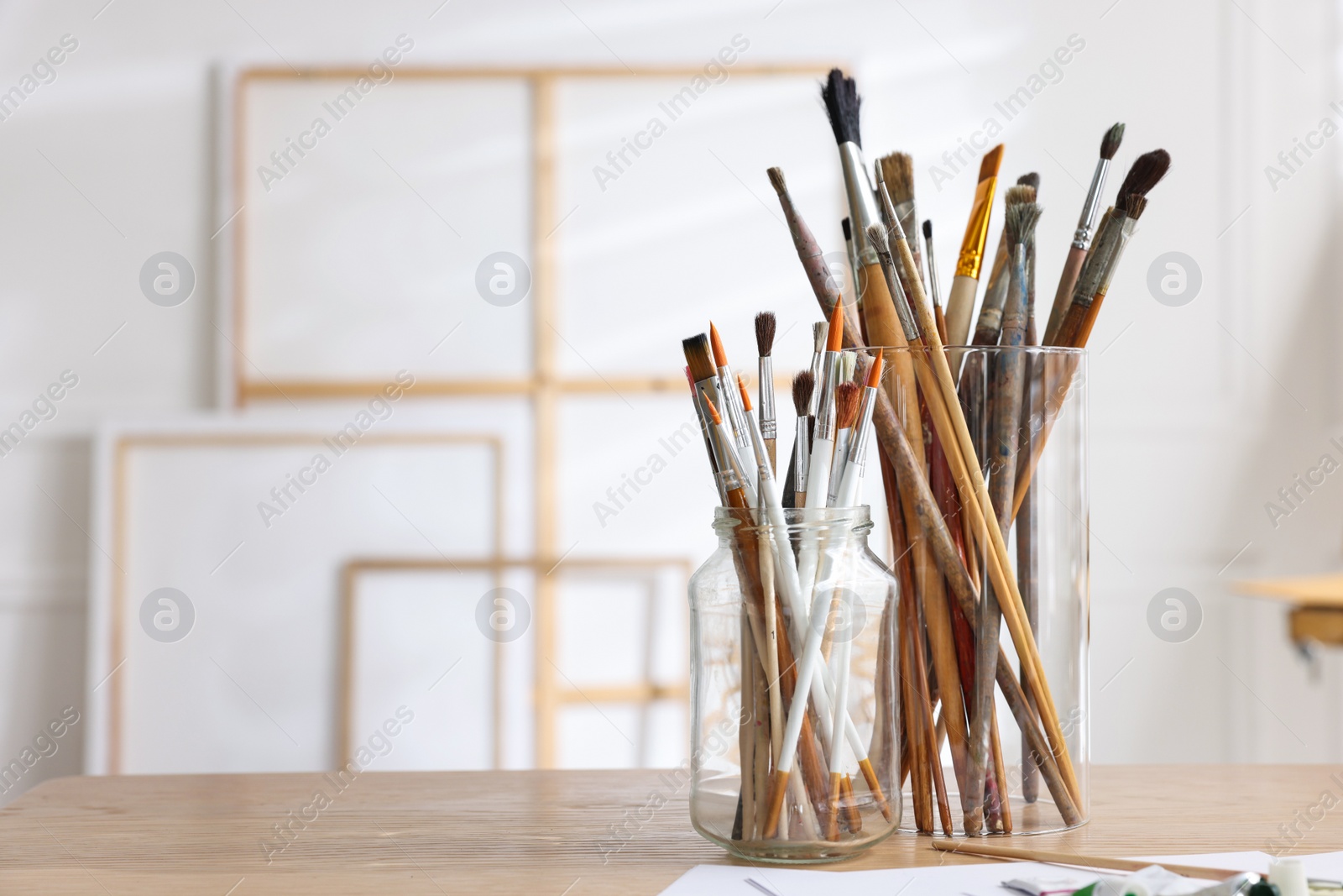 Photo of Holders with different paintbrushes on wooden table in studio, space for text. Artist's workplace