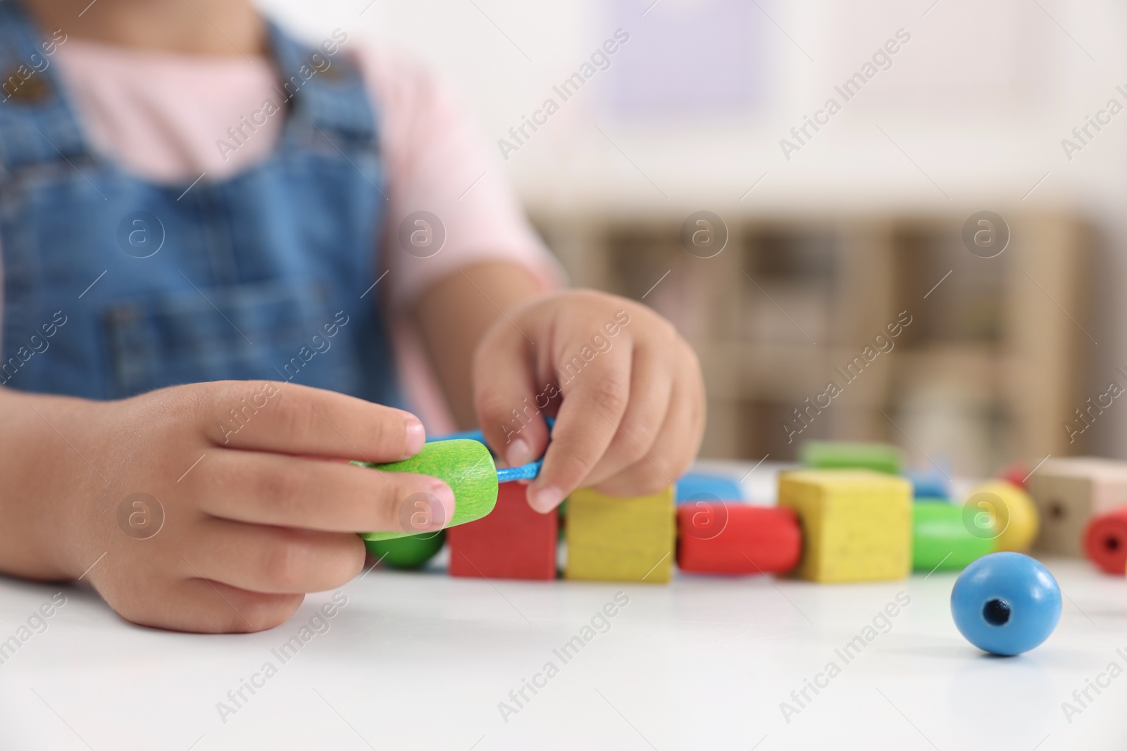 Photo of Motor skills development. Little girl playing with wooden pieces and string for threading activity at table indoors, closeup