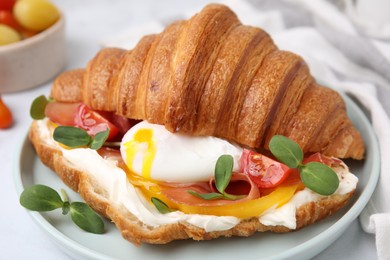 Photo of Tasty croissant with fried egg, tomato and microgreens on white table, closeup