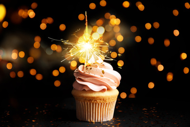 Image of Delicious birthday cupcake with sparkler on black table against blurred lights