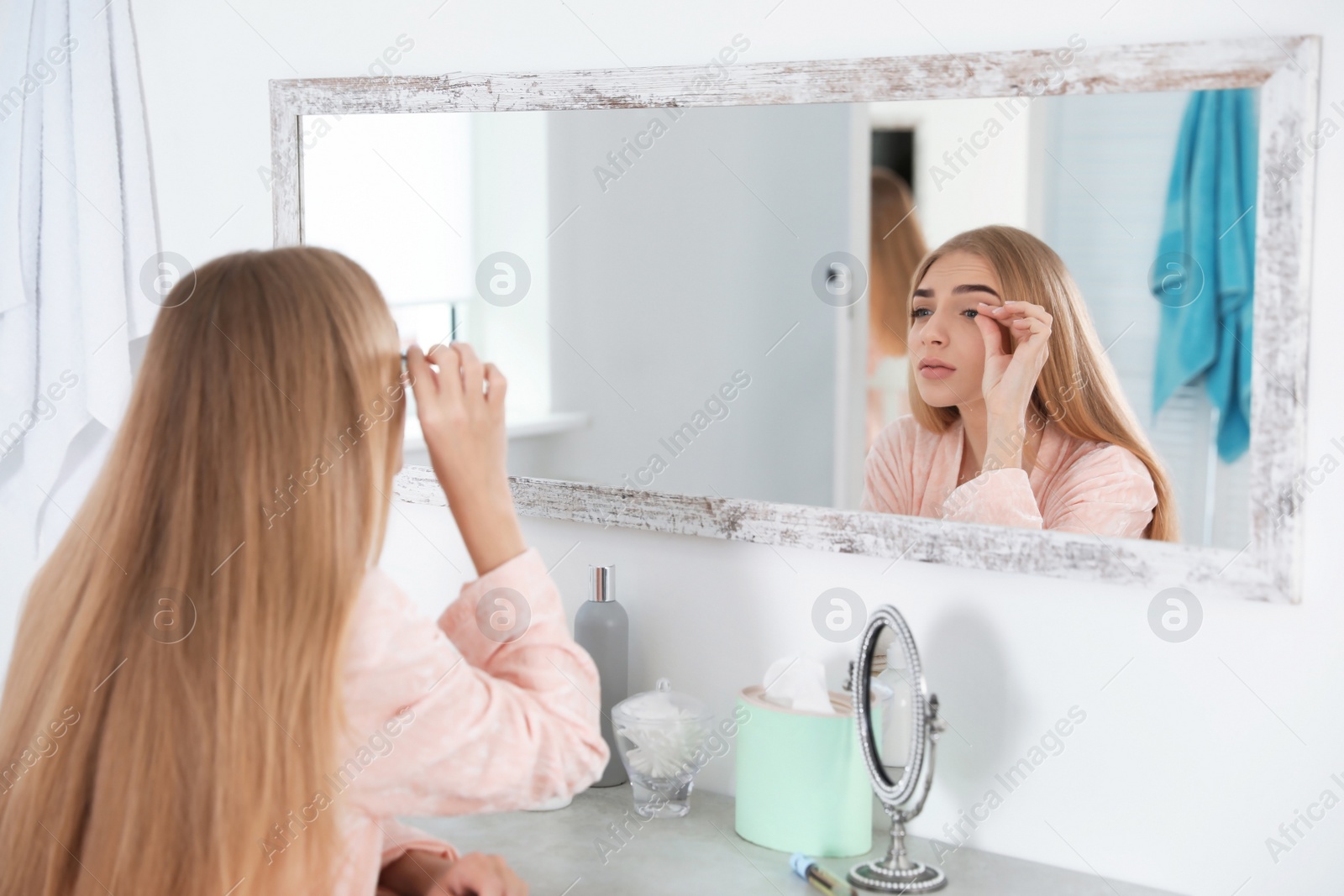 Photo of Young woman with eyelash loss problem looking in mirror indoors