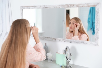 Photo of Young woman with eyelash loss problem looking in mirror indoors