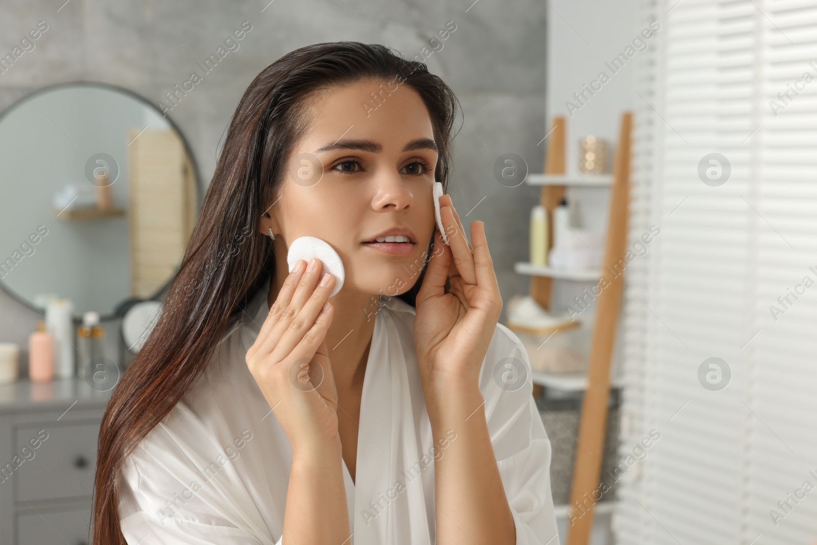 Photo of Young woman cleaning her face with cotton pads in bathroom