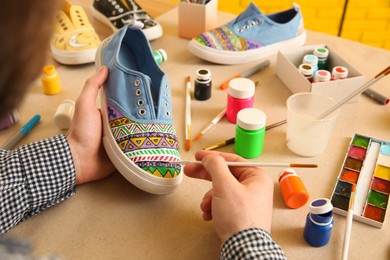 Photo of Man painting on sneaker at table, closeup. Customized shoes