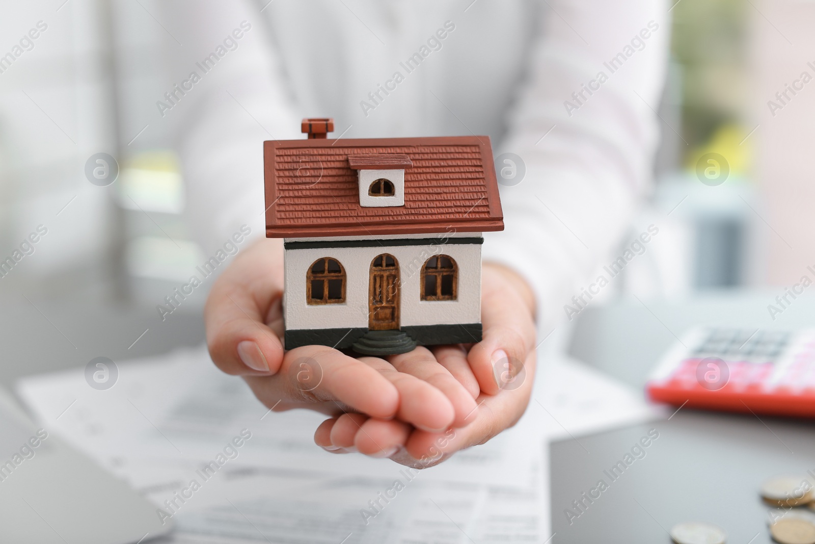 Photo of Woman holding house model on blurred background, closeup. Property tax