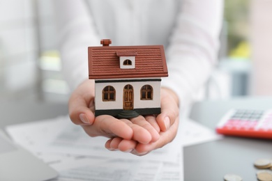 Photo of Woman holding house model on blurred background, closeup. Property tax