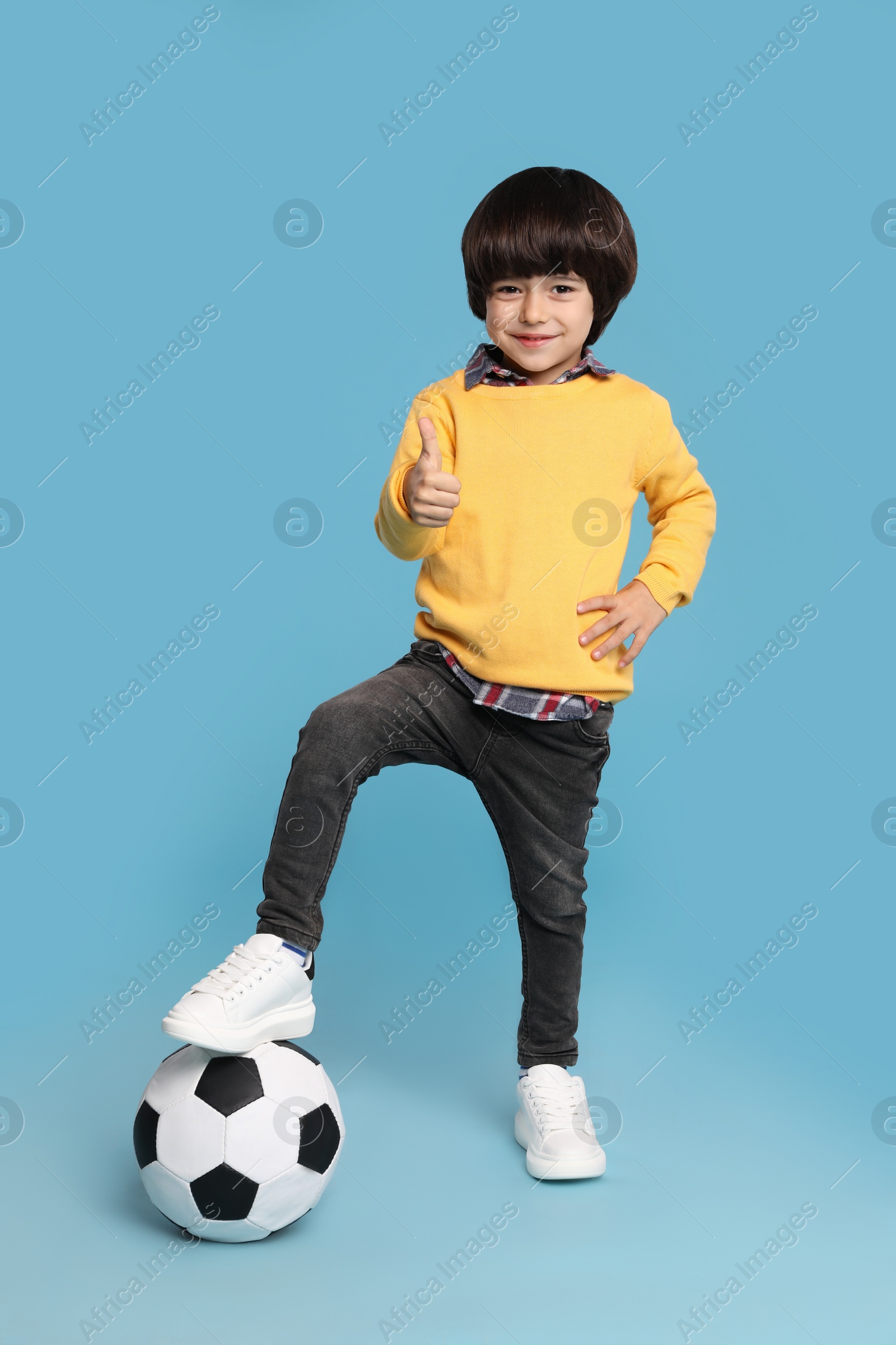 Photo of Cute little boy with soccer ball on light blue background
