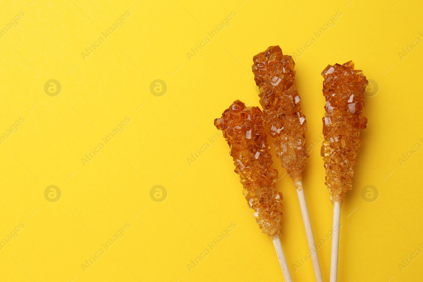 Photo of Wooden sticks with sugar crystals and space for text on yellow background, flat lay. Tasty rock candies