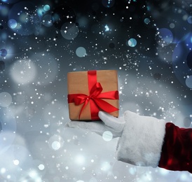 Image of Santa Claus holding gift box on winter background, bokeh effect