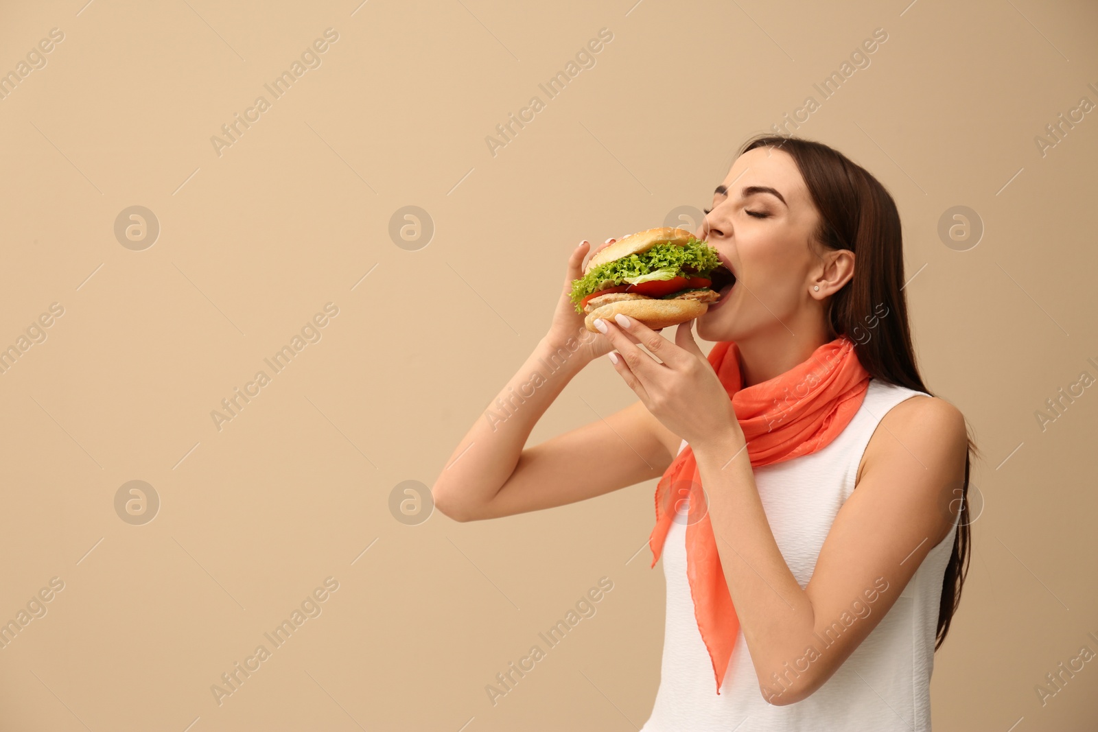 Photo of Young woman eating tasty burger on color background. Space for text