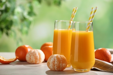 Photo of Delicious tangerine juice and fresh fruits on table against blurred background, space for text