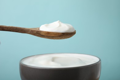 Photo of Eating delicious natural yogurt on light blue background, closeup