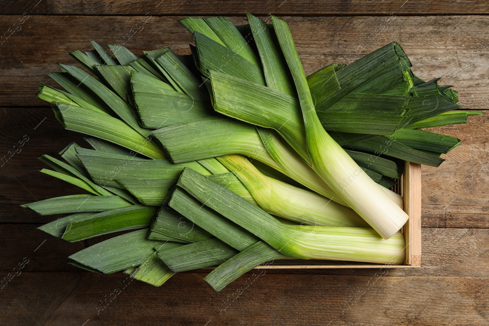 Photo of Crate with fresh raw leeks on wooden table, top view. Ripe onion