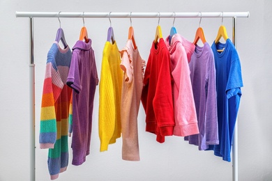 Photo of Colorful clothes hanging on wardrobe rack against light background