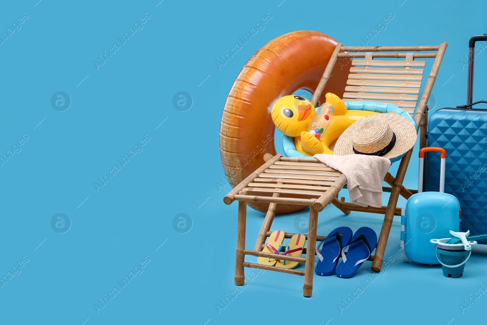 Photo of Deck chair, suitcases and beach accessories on light blue background, space for text. Summer vacation