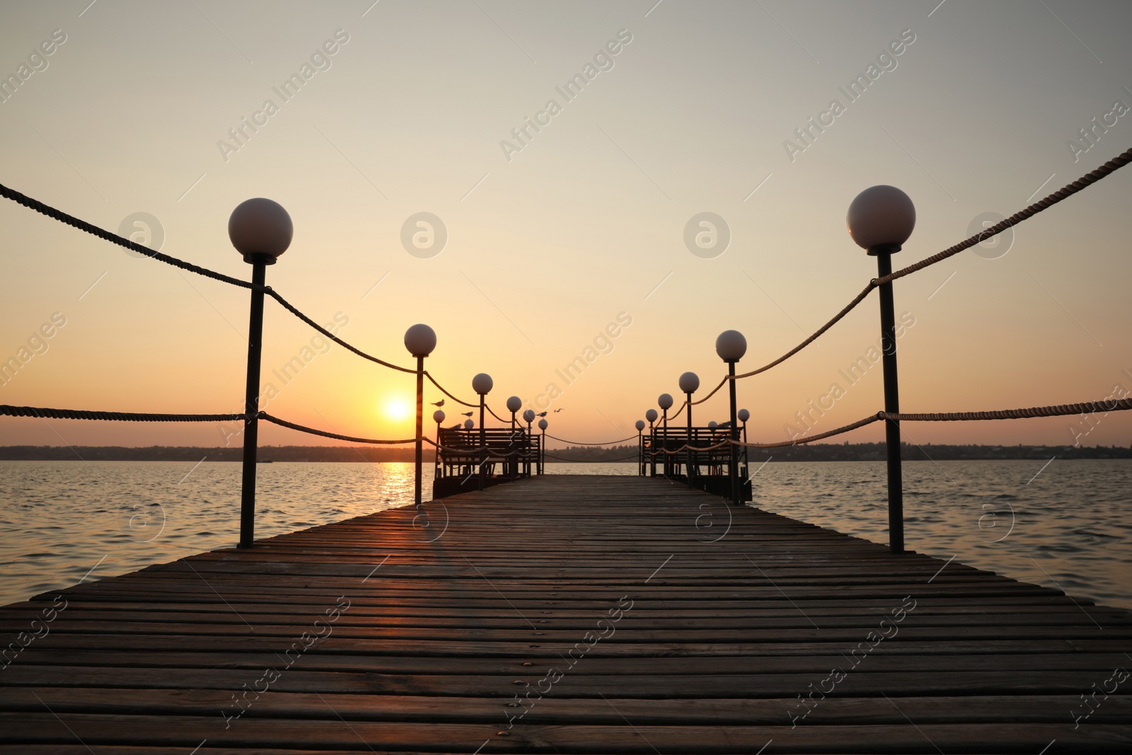 Photo of Picturesque view of empty wooden pier with lanterns at sunset