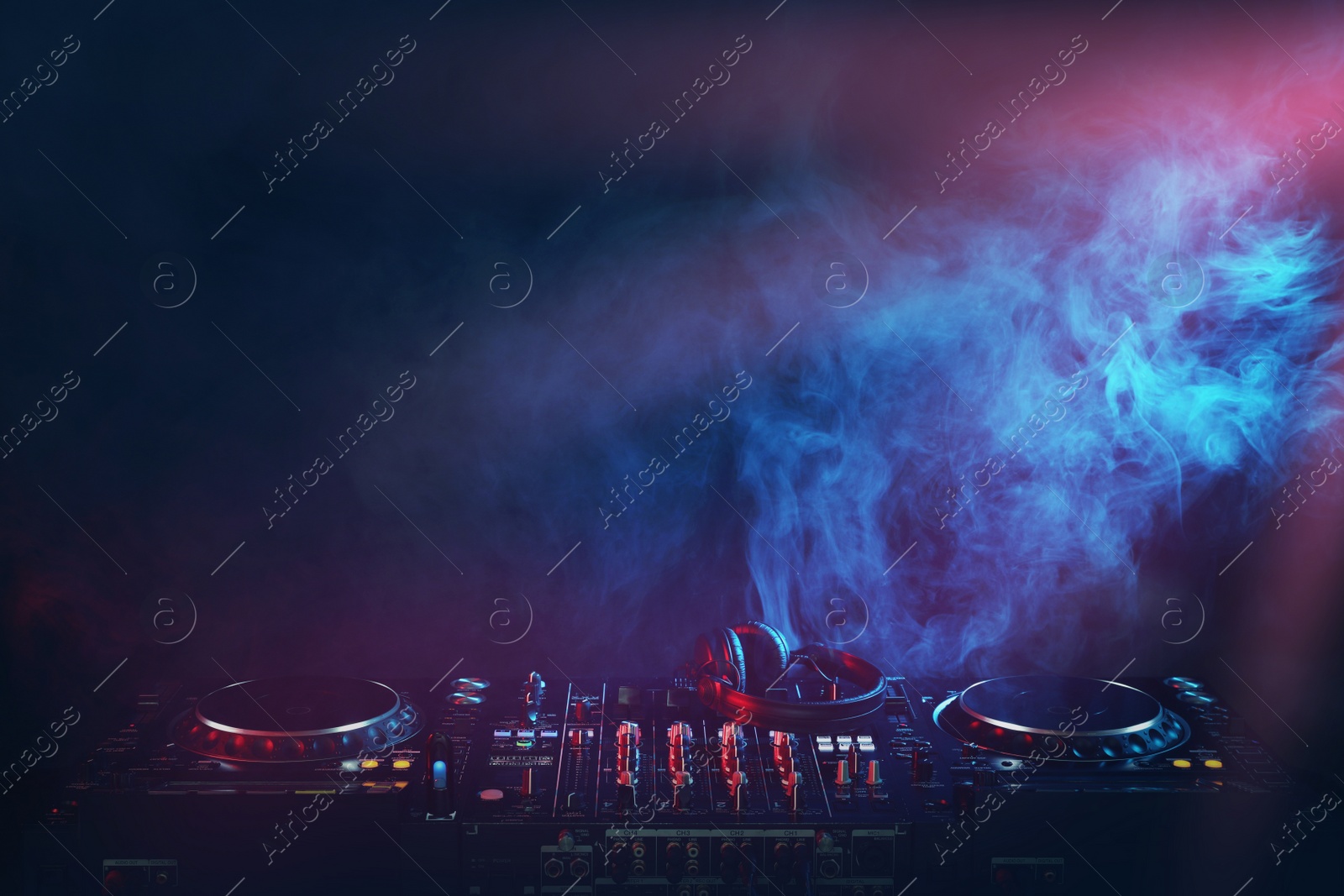 Photo of Modern DJ controller and headphones on dark background with smoke. Space for text
