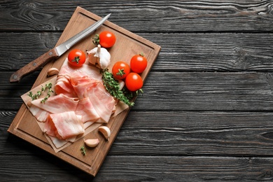 Photo of Board with raw bacon rashers, tomatoes and garlic on wooden background