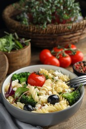 Photo of Bowl of delicious pasta with tomatoes, olives and broccoli on wooden table