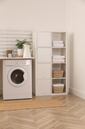 Photo of Laundry room interior with modern washing machine and shelving unit near white wall