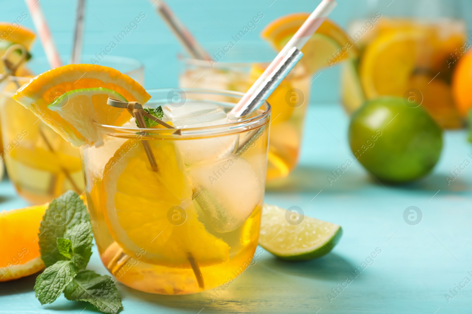 Photo of Delicious refreshing drink with orange and lime slices on light blue table, closeup