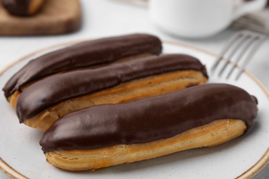 Photo of Delicious eclairs covered with chocolate on plate, closeup