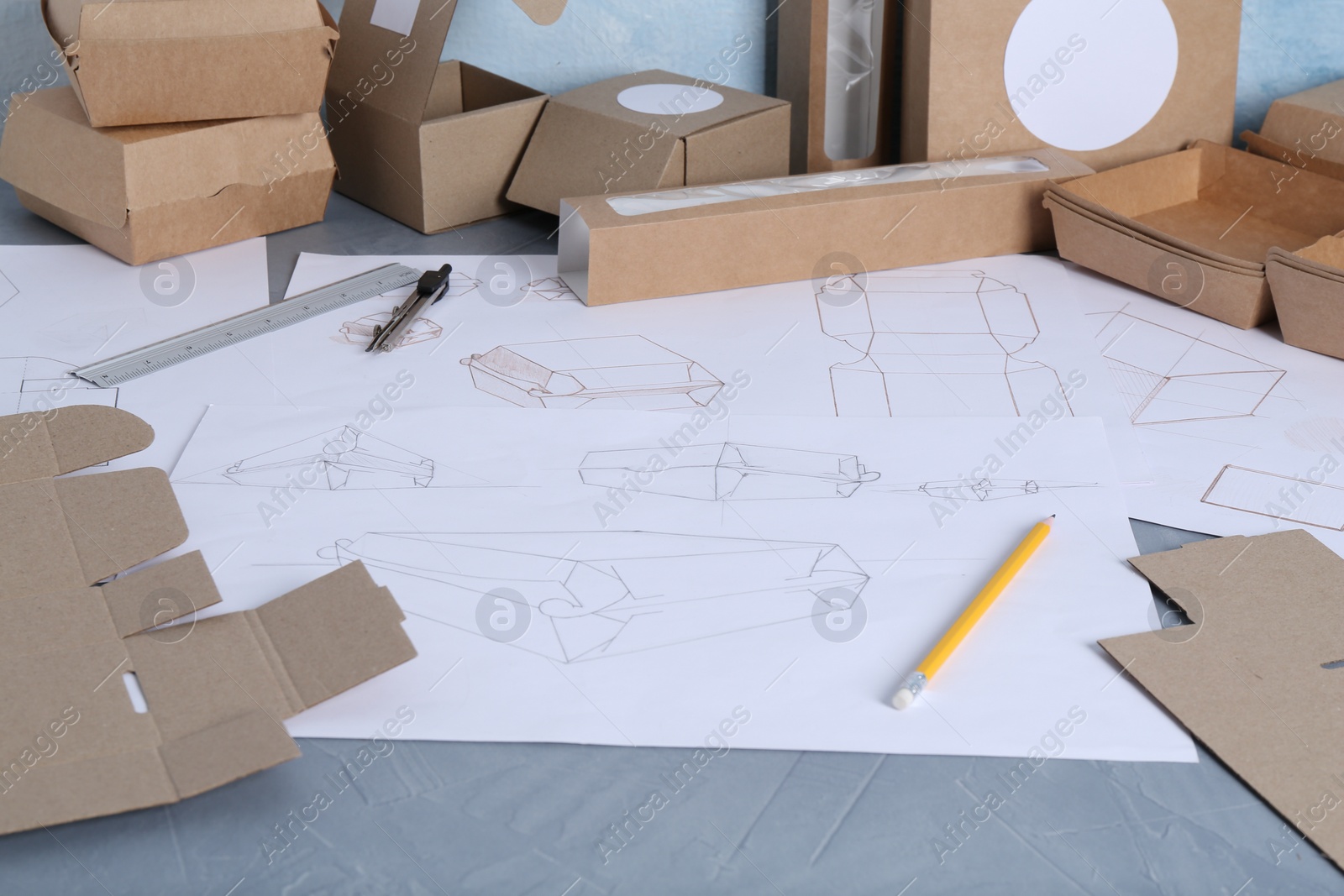 Photo of Creating packaging design. Drawings, boxes and stationery on blue textured table, closeup