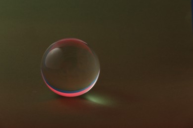 Photo of Transparent glass ball on dark olive background. Space for text