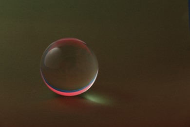 Transparent glass ball on dark olive background. Space for text