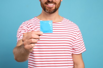 Happy man holding condom on light blue background. Safe sex