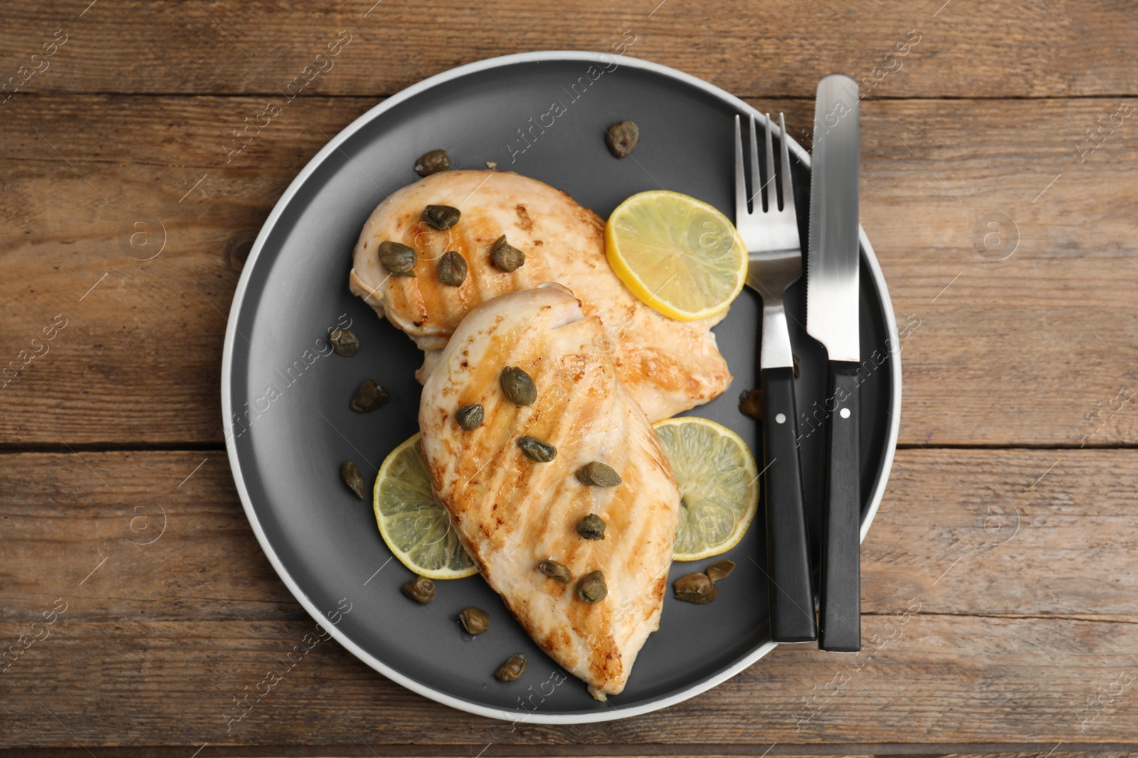 Photo of Delicious chicken fillets with capers and lemon served on wooden table, top view