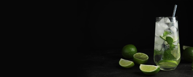 Image of Tasty refreshing soda drink with ice cubes, lime slices and mint on black table. Banner design with space for text