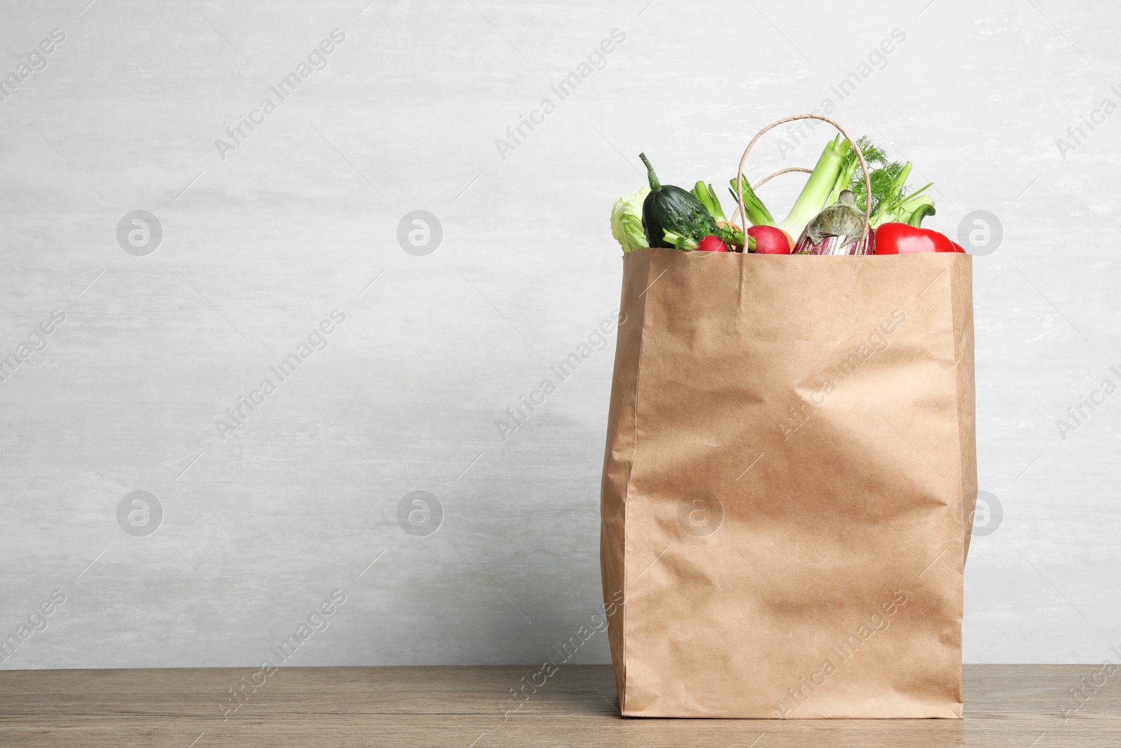 Photo of Paper bag with vegetables on table against grey background. Space for text