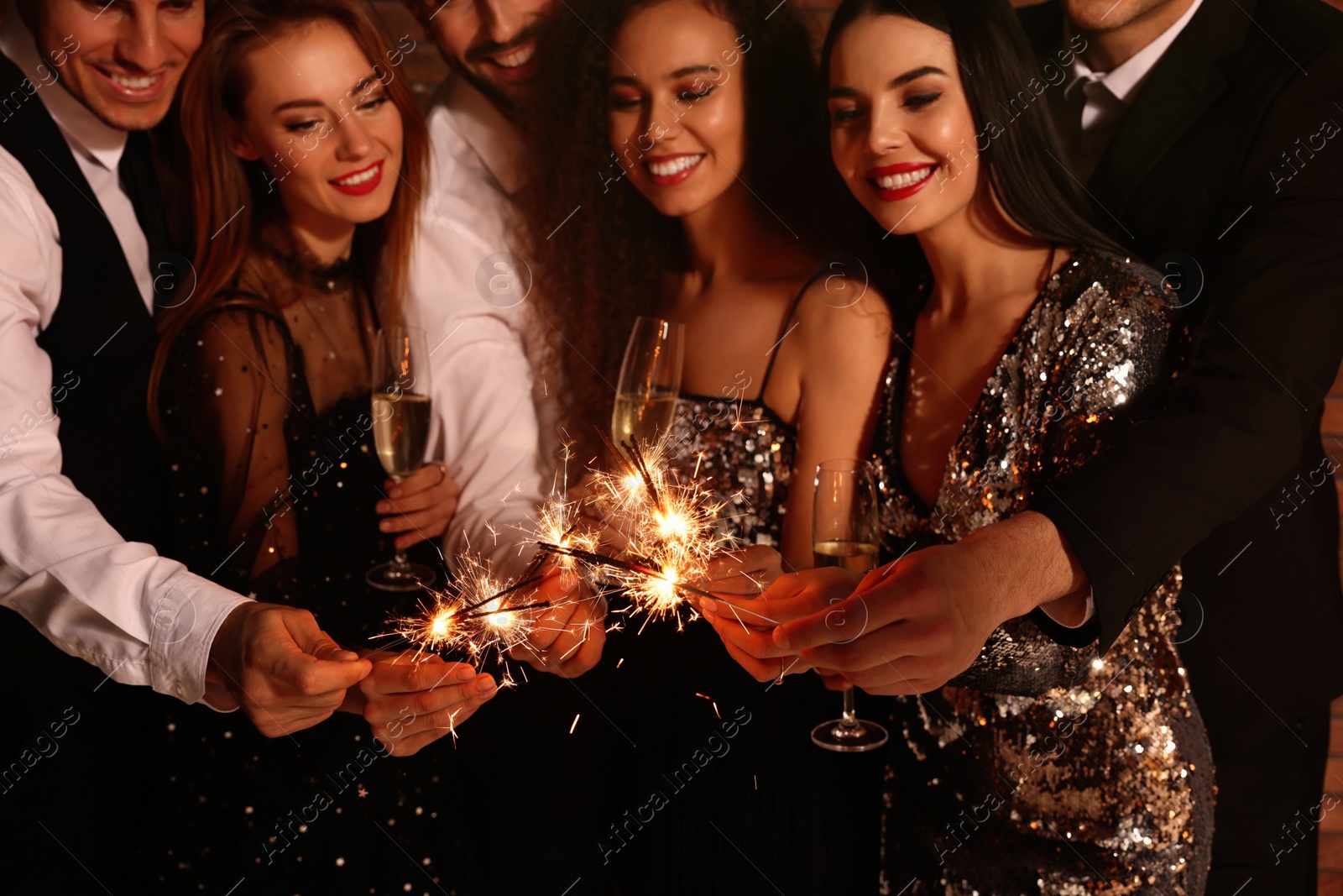 Photo of Happy friends with glasses of sparkling wine and sparklers celebrating New Year, focus on hands