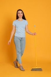 Beautiful young woman with broom on yellow background