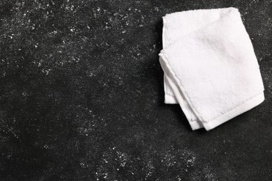 Photo of Soft folded terry towel on black textured background, top view. Space for text