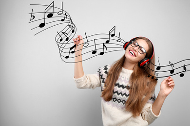 Young woman listening to music with headphones on light background