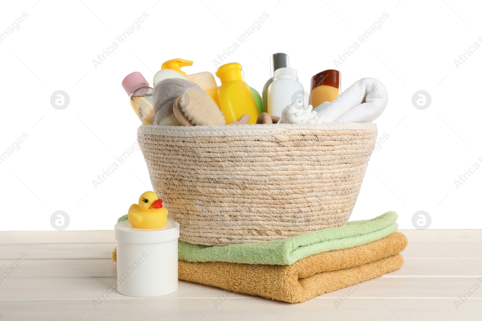 Photo of Wicker basket full of different baby cosmetic products, bathing accessories and toys on wooden table against white background