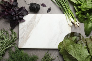 Different herbs and marble cutting board on grey table, flat lay. Space for text