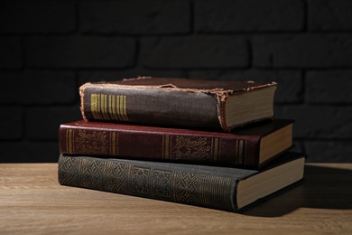 Stack of old hardcover books on wooden table near black wall