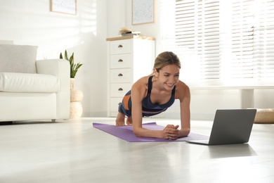 Photo of Woman having online video class via laptop at home. Distance yoga course during coronavirus pandemic