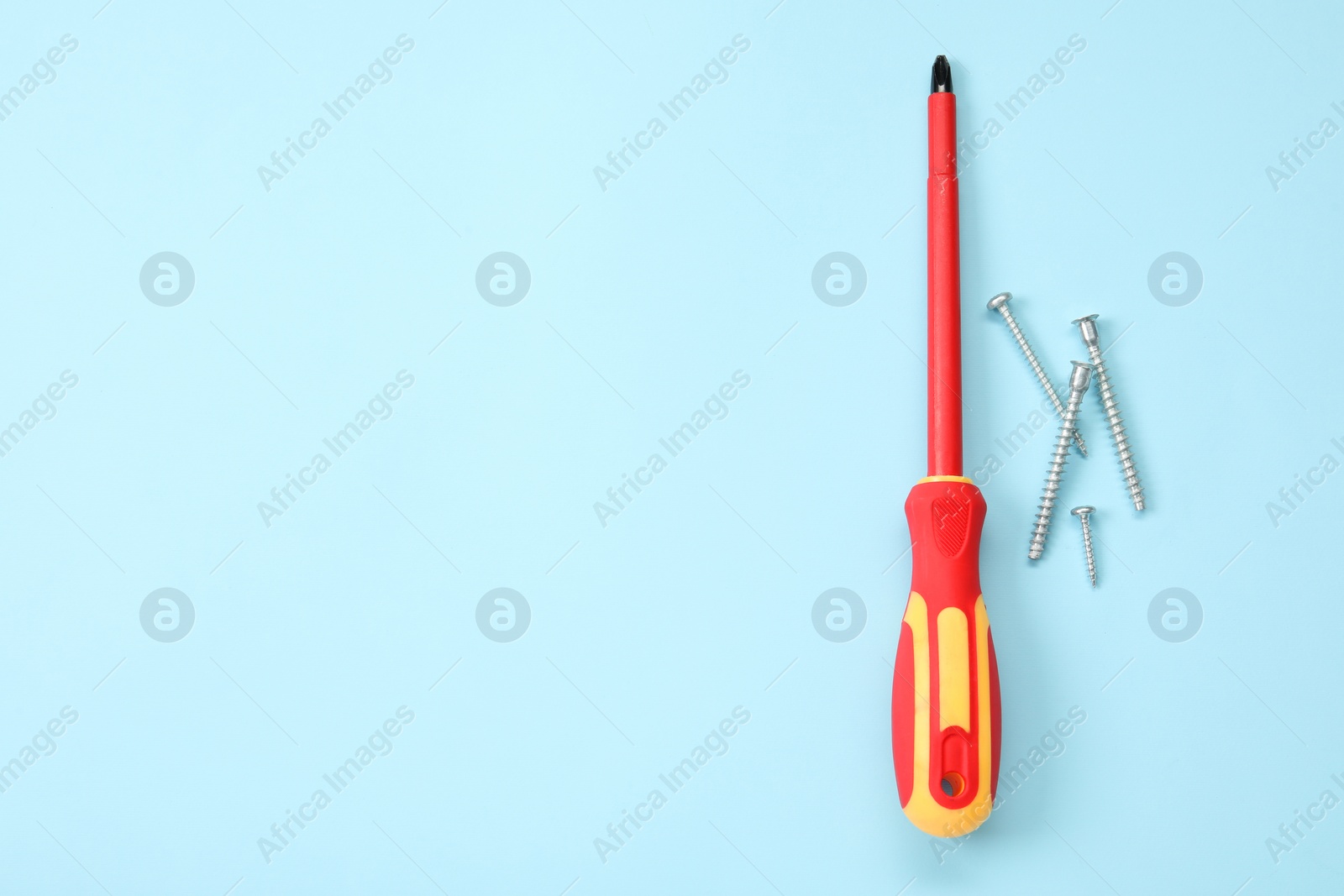 Photo of Screwdriver with red handle and screws on light blue background, flat lay. Space for text