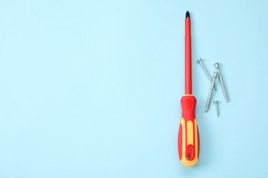 Photo of Screwdriver with red handle and screws on light blue background, flat lay. Space for text