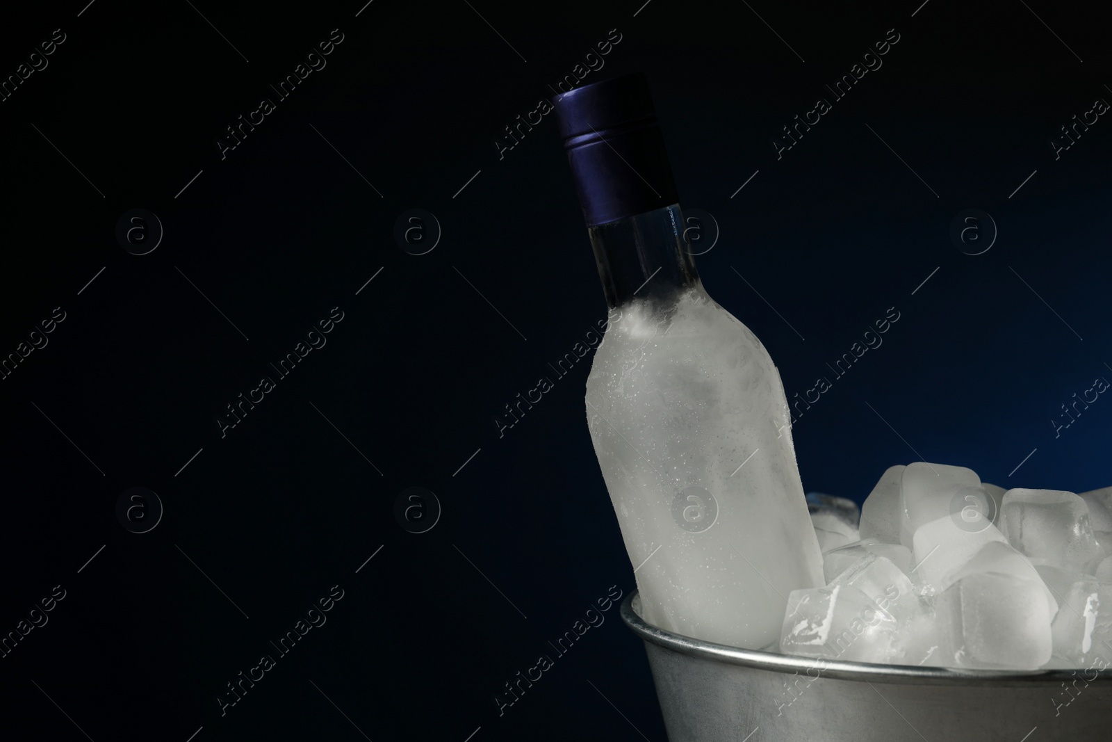 Photo of Bottle of vodka in metal bucket with ice on dark background. Space for text