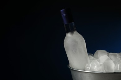 Photo of Bottle of vodka in metal bucket with ice on dark background. Space for text