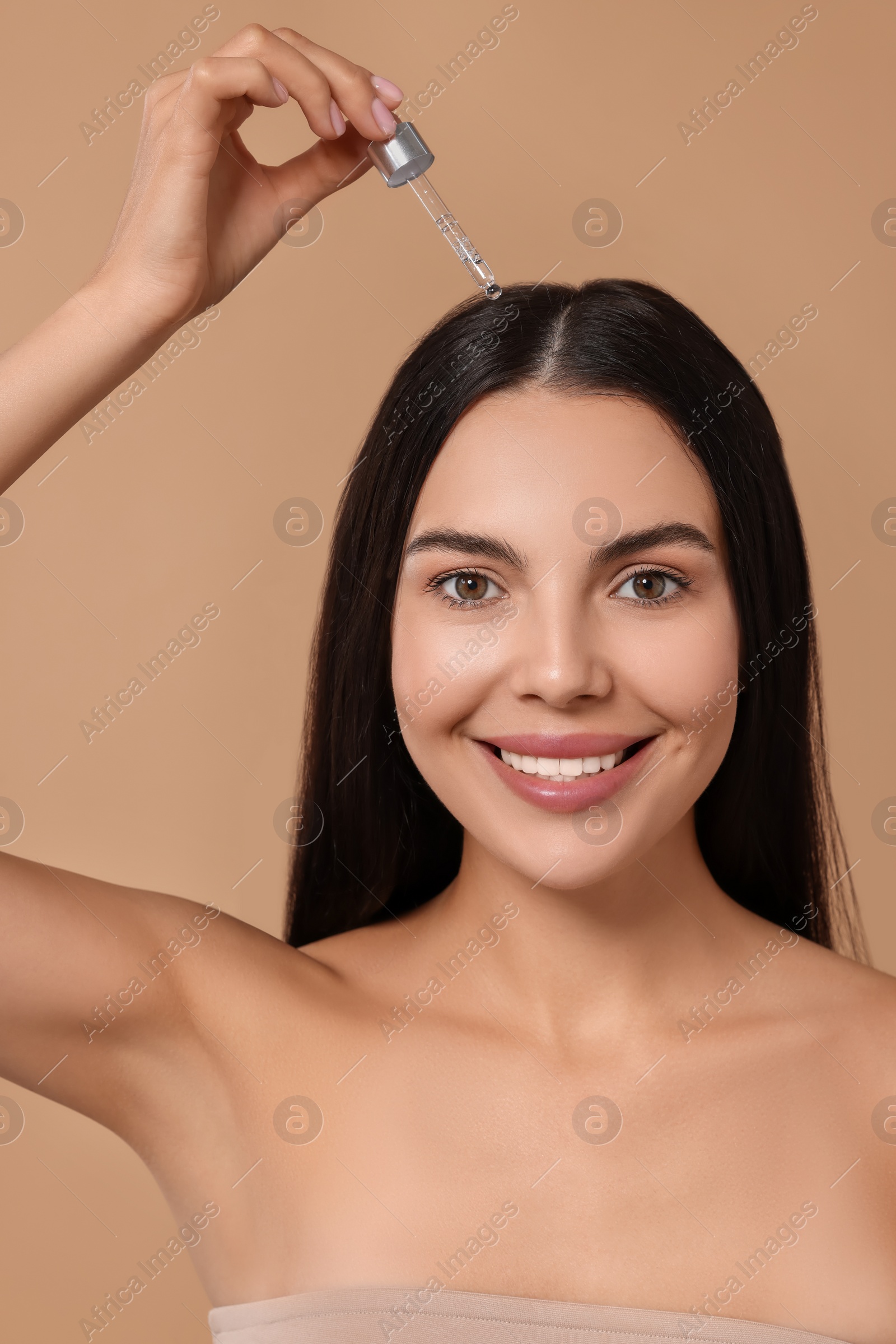 Photo of Beautiful woman applying hair serum on beige background. Cosmetic product