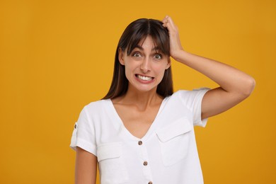 Embarrassed woman scratching head on orange background